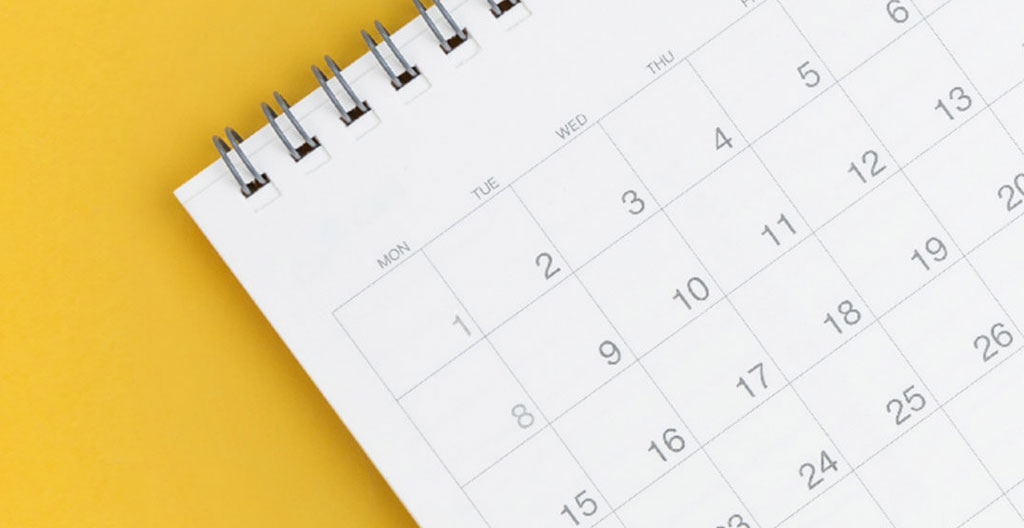 Gros plan sur un calendrier mural moderne avec des dates encerclées au marqueur rouge, main tenant un stylo, mise au point sélective